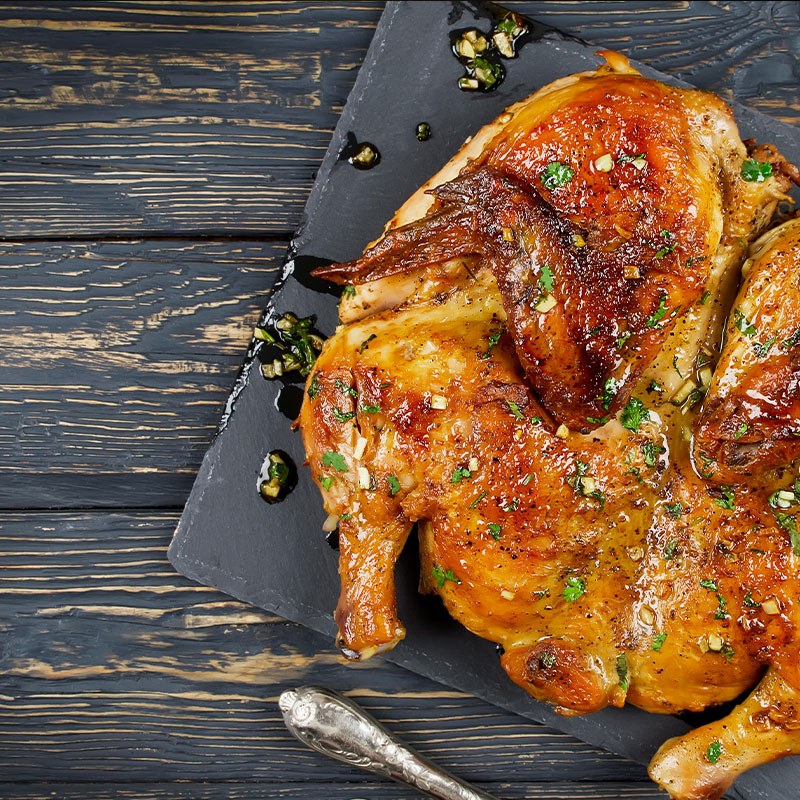 Spatchcocked Roasted Chicken On Slate with A Wood Background